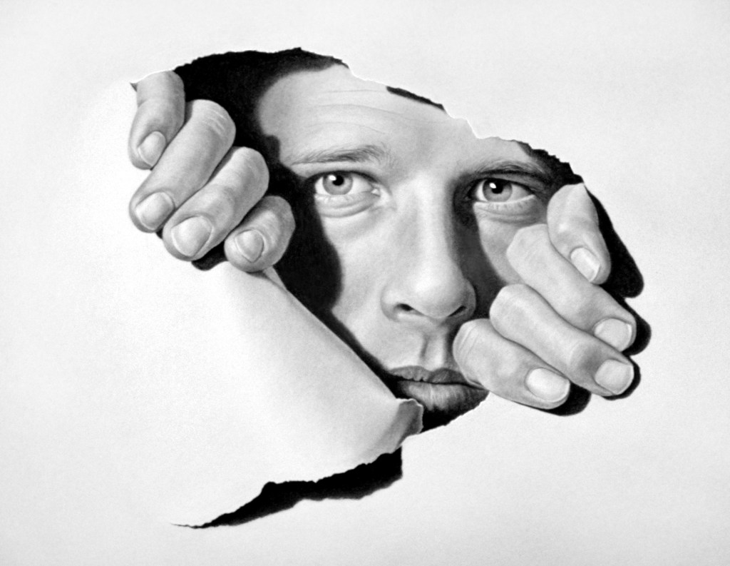 A drawing of a person peers through a torn piece of paper, with only their face and hands visible. Their fingers grasp the edges of the tear, appearing to emerge from the blank white background. The expression on their face is one of curiosity and intent focus. Artist JD Hillberry.